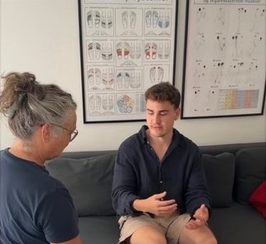 Samtale i klinikken på sofaen foran plancher over reflekszoner